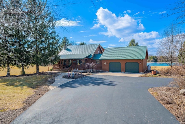 chalet / cabin with covered porch, an attached garage, a front yard, metal roof, and driveway