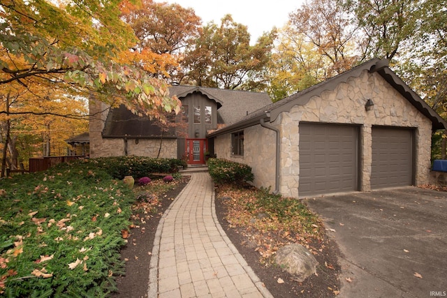 view of front of property featuring a shingled roof, stone siding, driveway, and an attached garage