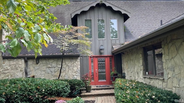 doorway to property featuring board and batten siding, stone siding, and roof with shingles