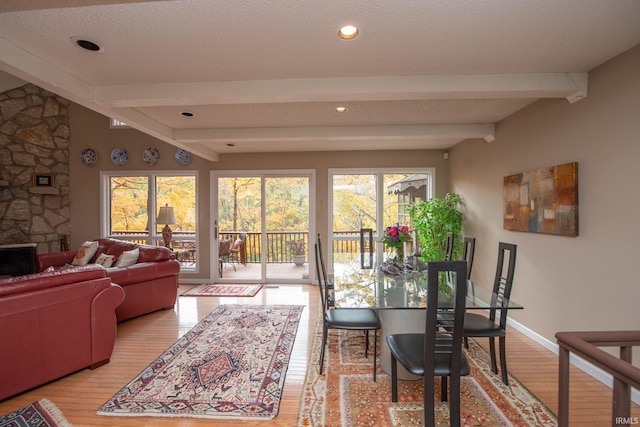 living area with beamed ceiling, a stone fireplace, baseboards, and wood finished floors