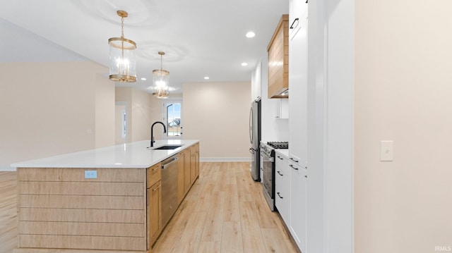 kitchen with a sink, light countertops, appliances with stainless steel finishes, a large island, and light wood-type flooring