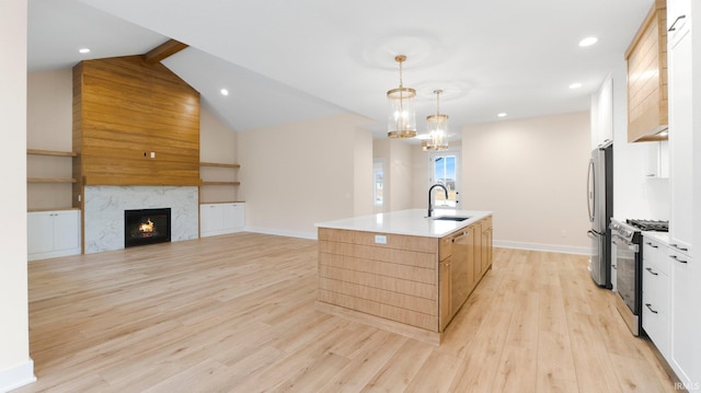 kitchen featuring light wood-style flooring, appliances with stainless steel finishes, a high end fireplace, a kitchen island with sink, and a sink