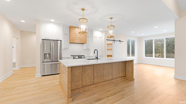 kitchen with a barn door, a center island with sink, decorative backsplash, light wood-type flooring, and stainless steel refrigerator with ice dispenser