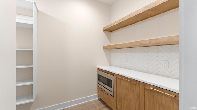 bar with baseboards, stainless steel microwave, backsplash, and light wood finished floors