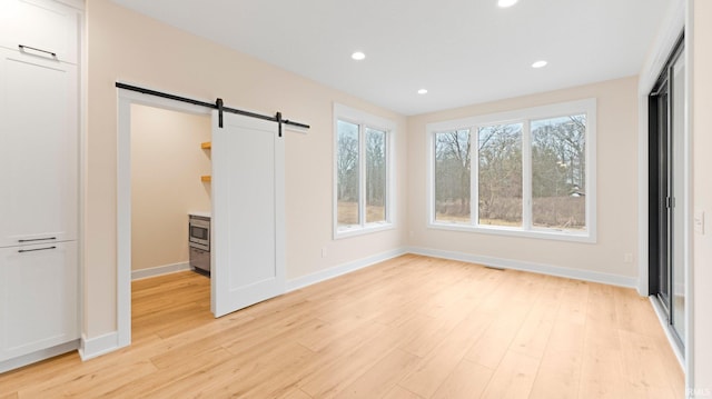 unfurnished bedroom featuring light wood-type flooring, baseboards, recessed lighting, and a barn door