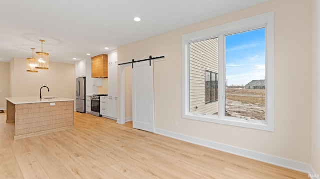 kitchen featuring stainless steel appliances, light countertops, light wood-style flooring, a barn door, and a sink