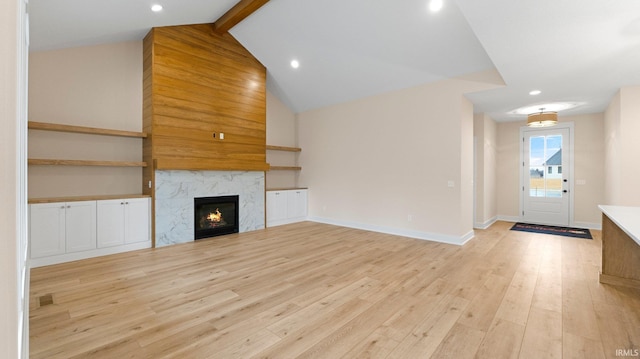 unfurnished living room featuring baseboards, a high end fireplace, beamed ceiling, light wood-style floors, and recessed lighting