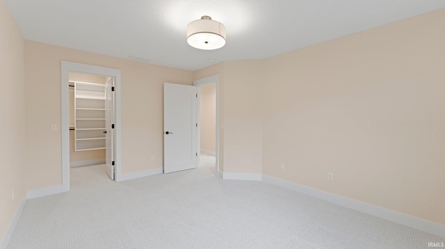 unfurnished bedroom featuring a walk in closet, a closet, baseboards, and carpet