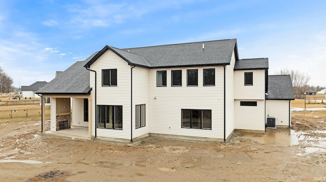 rear view of house with a shingled roof, a patio area, central AC, and fence