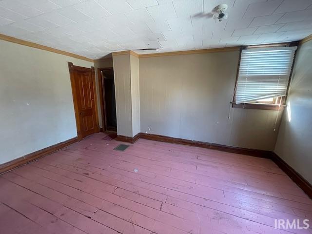 empty room with ornamental molding, baseboards, visible vents, and hardwood / wood-style floors