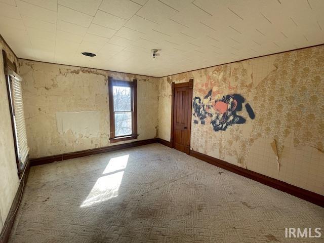 empty room with carpet flooring, baseboards, and wallpapered walls