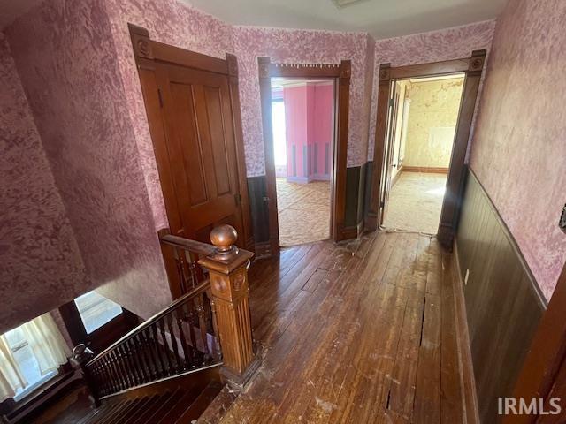 corridor with wallpapered walls, hardwood / wood-style floors, and an upstairs landing