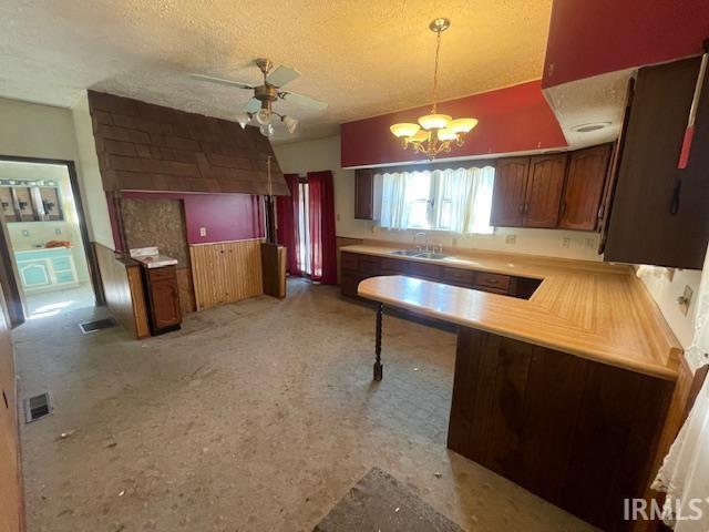 kitchen with light countertops, a sink, a textured ceiling, a peninsula, and ceiling fan with notable chandelier