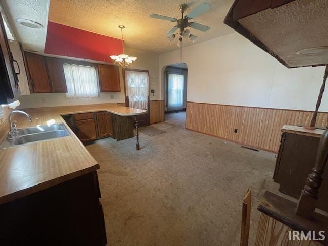 kitchen with arched walkways, a textured ceiling, a sink, light countertops, and wainscoting