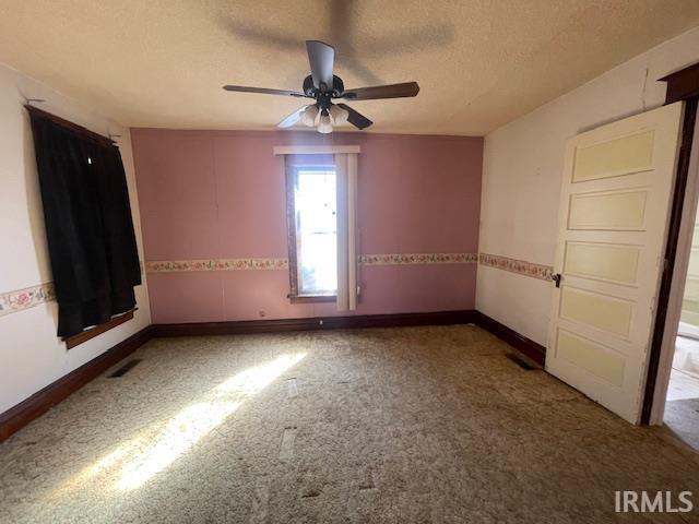 carpeted spare room featuring a ceiling fan, visible vents, baseboards, and a textured ceiling