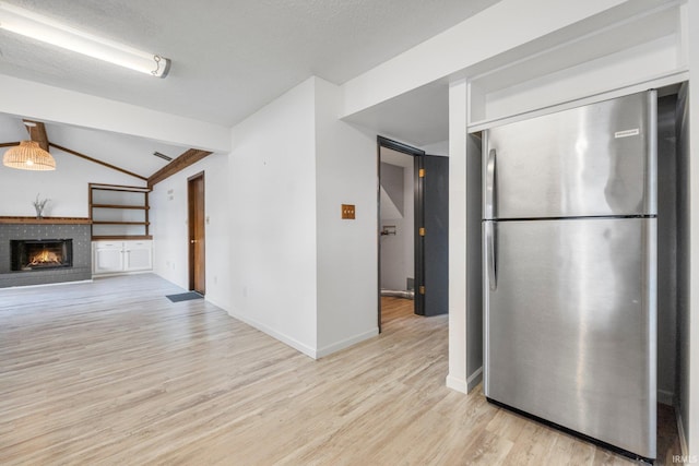 kitchen with baseboards, lofted ceiling with beams, light wood-style flooring, freestanding refrigerator, and a fireplace