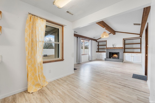 unfurnished living room with baseboards, visible vents, lofted ceiling with beams, wood finished floors, and a brick fireplace