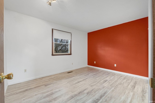 spare room featuring wood finished floors, visible vents, and baseboards