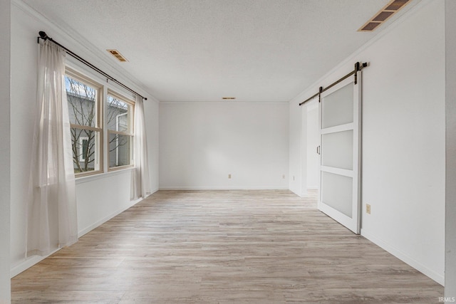 empty room with light wood-type flooring, visible vents, a textured ceiling, and a barn door