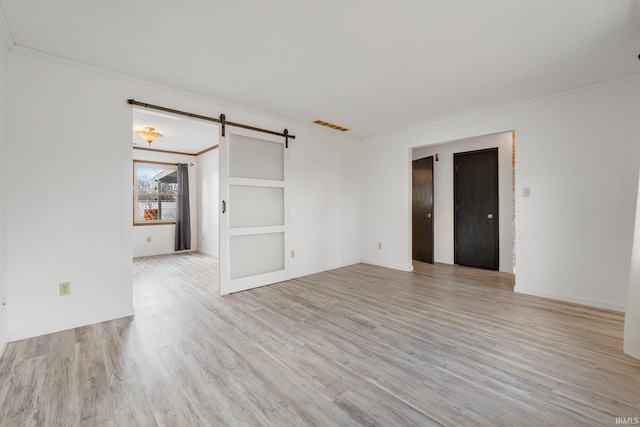 spare room with a barn door, visible vents, baseboards, ornamental molding, and light wood finished floors