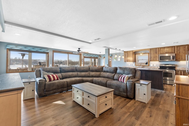 living room with a textured ceiling, dark wood-type flooring, visible vents, and recessed lighting