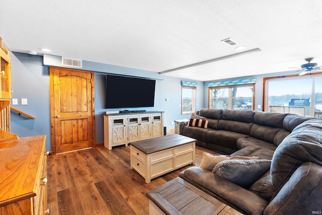 living room with a textured ceiling, dark wood finished floors, visible vents, and a ceiling fan