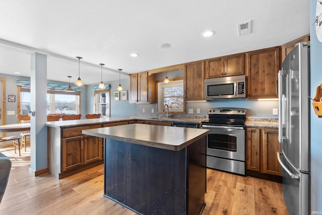 kitchen with brown cabinetry, appliances with stainless steel finishes, a peninsula, light wood-type flooring, and a sink