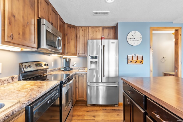 kitchen with a textured ceiling, light wood-style flooring, visible vents, appliances with stainless steel finishes, and brown cabinetry