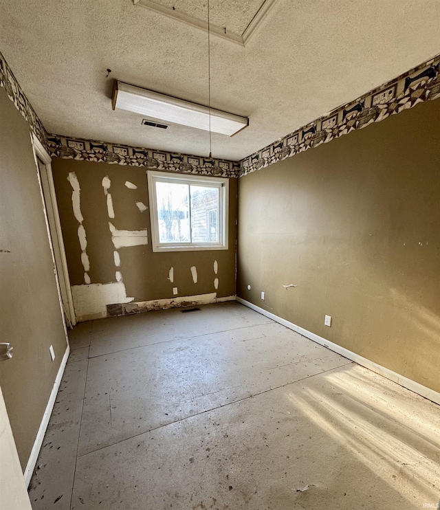 empty room featuring attic access, visible vents, a textured ceiling, and baseboards