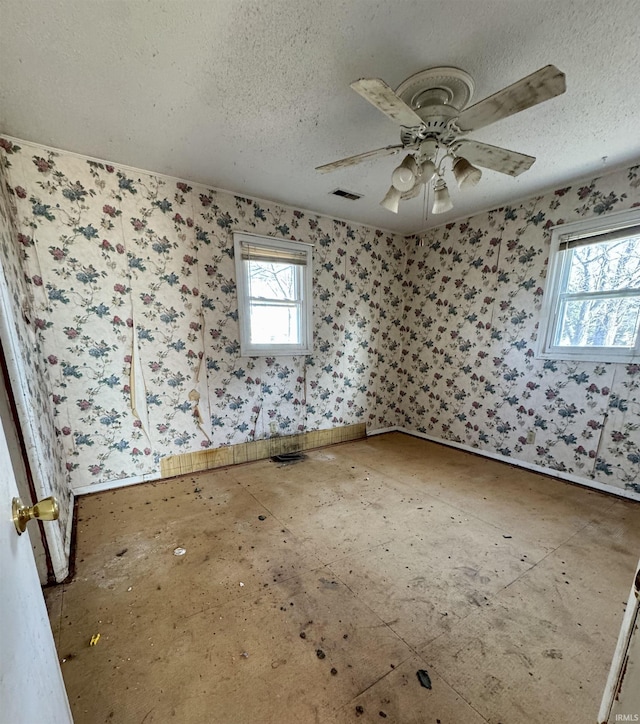 spare room with a healthy amount of sunlight, visible vents, a textured ceiling, and wallpapered walls