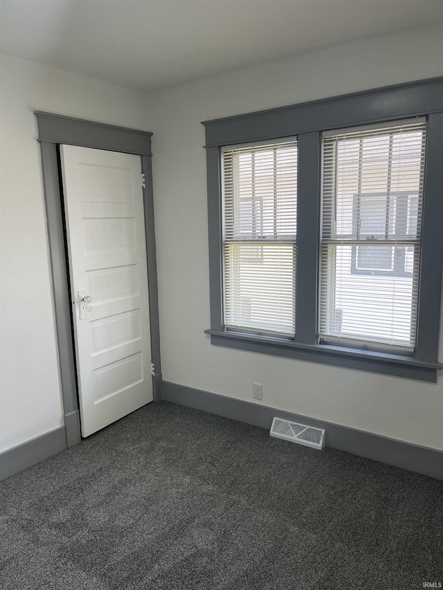 unfurnished room with baseboards, visible vents, and dark carpet