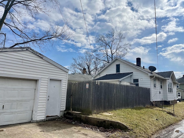 view of home's exterior featuring a garage, concrete driveway, fence, and an outdoor structure