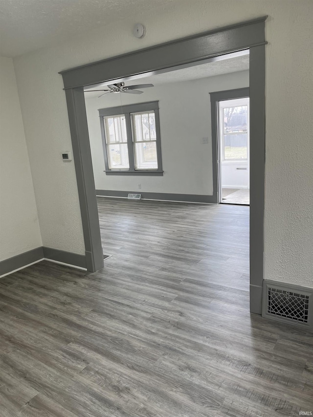 empty room featuring a ceiling fan, wood finished floors, visible vents, and baseboards