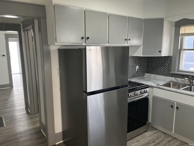 kitchen with wood finished floors, a sink, light countertops, appliances with stainless steel finishes, and tasteful backsplash
