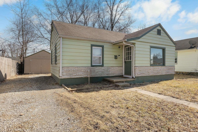 view of front of house featuring a storage shed, stone siding, roof with shingles, fence, and an outdoor structure