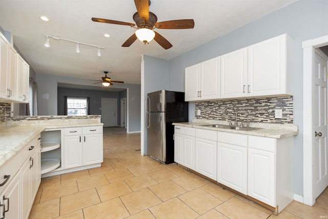 kitchen featuring a peninsula, a sink, white cabinetry, freestanding refrigerator, and decorative backsplash