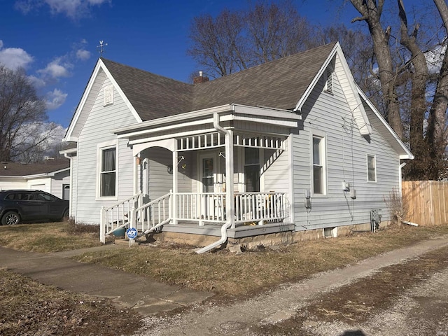 view of front of home featuring covered porch, roof with shingles, a chimney, and fence