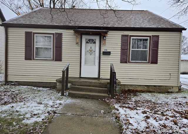 bungalow-style home with entry steps and roof with shingles