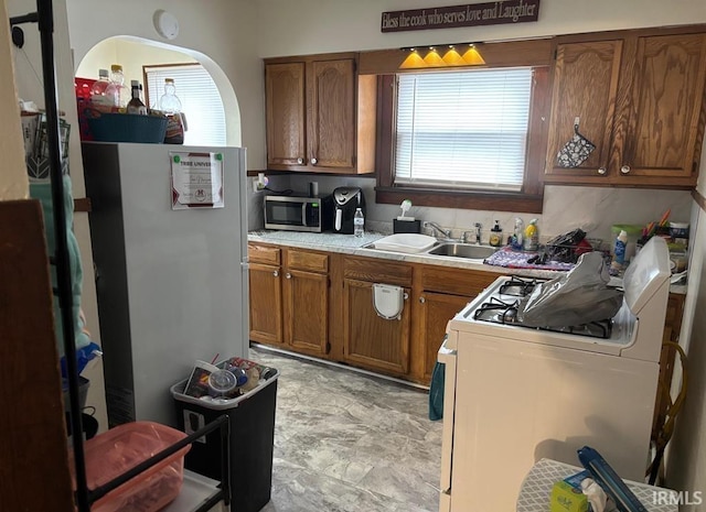 kitchen with a sink, white range with gas cooktop, light countertops, brown cabinets, and stainless steel microwave