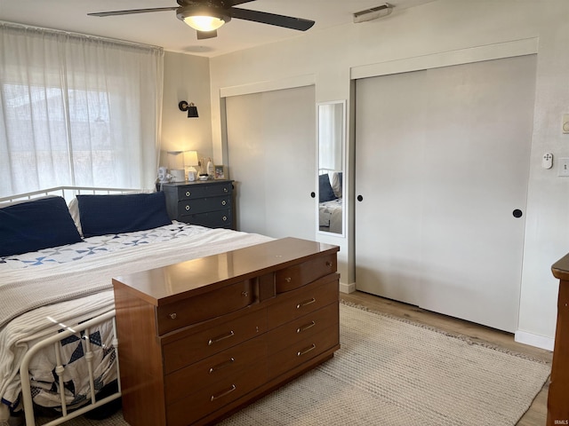 bedroom with multiple closets, a ceiling fan, visible vents, and wood finished floors