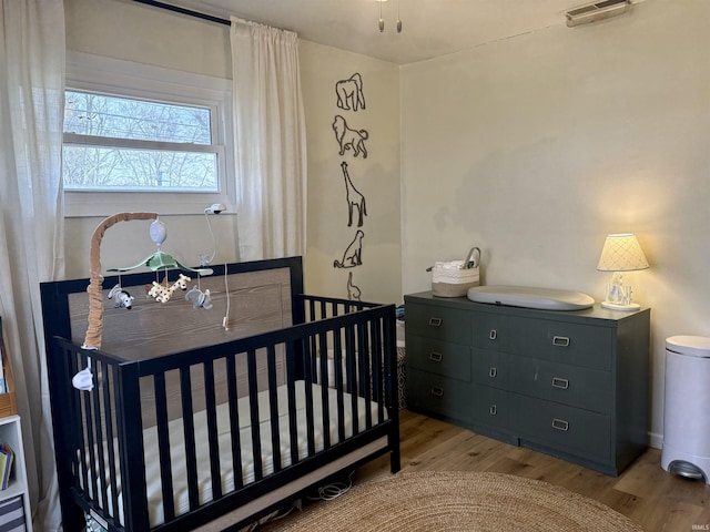 bedroom with light wood-type flooring and a nursery area