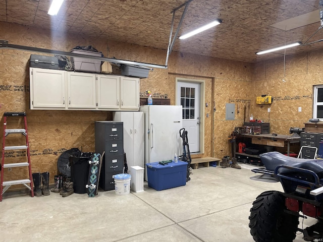 garage with a workshop area, freestanding refrigerator, and electric panel