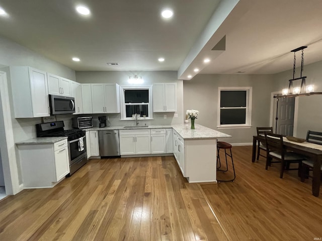 kitchen with light wood-style flooring, appliances with stainless steel finishes, white cabinetry, a peninsula, and a kitchen breakfast bar