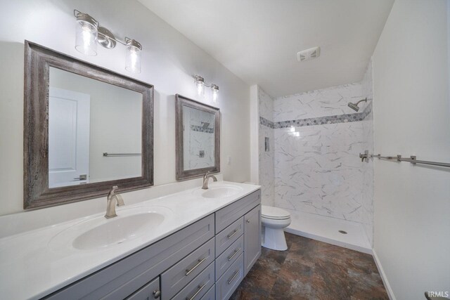 bathroom featuring a sink, a tile shower, toilet, and double vanity