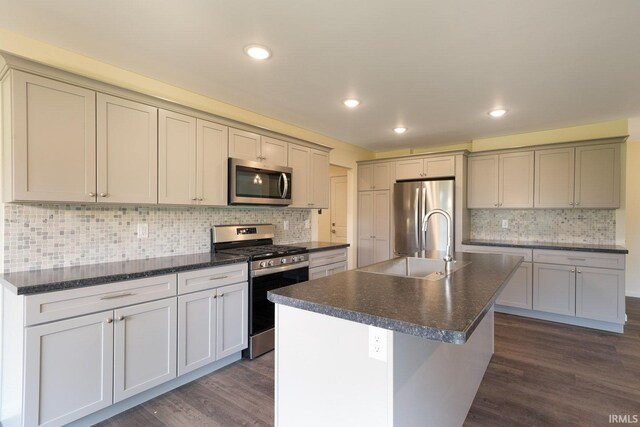 kitchen featuring dark countertops, dark wood-style floors, a center island with sink, and stainless steel appliances