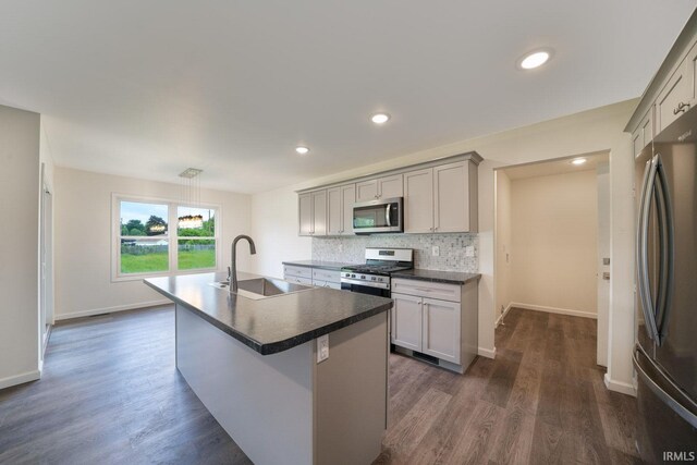 kitchen featuring gray cabinetry, a sink, appliances with stainless steel finishes, backsplash, and dark countertops