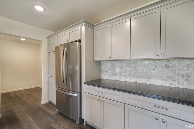 kitchen featuring dark wood-style flooring, decorative backsplash, freestanding refrigerator, dark stone countertops, and baseboards