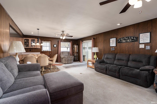 living area featuring light carpet, ceiling fan with notable chandelier, and wooden walls