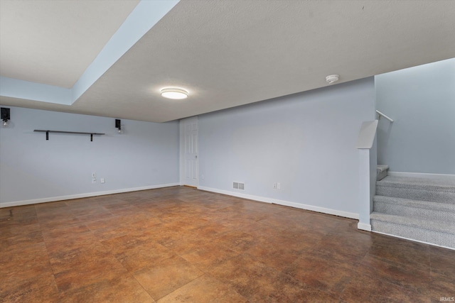 finished below grade area with visible vents, stairway, baseboards, and a textured ceiling