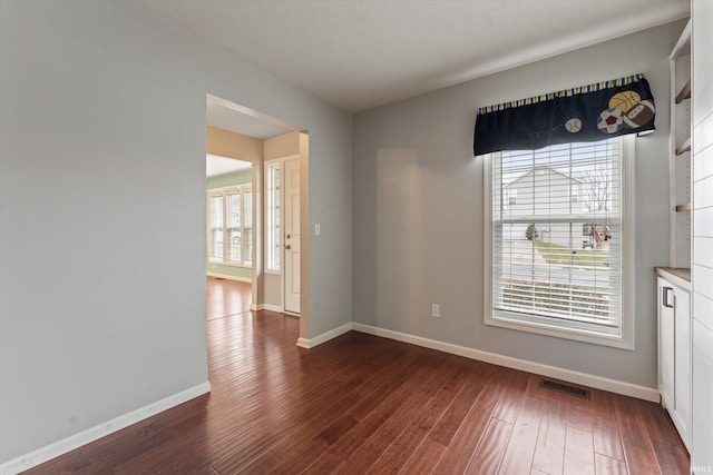 spare room featuring dark wood-style floors, visible vents, and baseboards